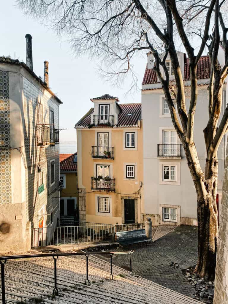 A quiet corner in Lisbon’s Alfama neighbourhood, with yellow and tiled houses, cobbled streets, and leafless trees casting morning shadows. A perfect scene for a photography workshop in Lisbon Alfama.