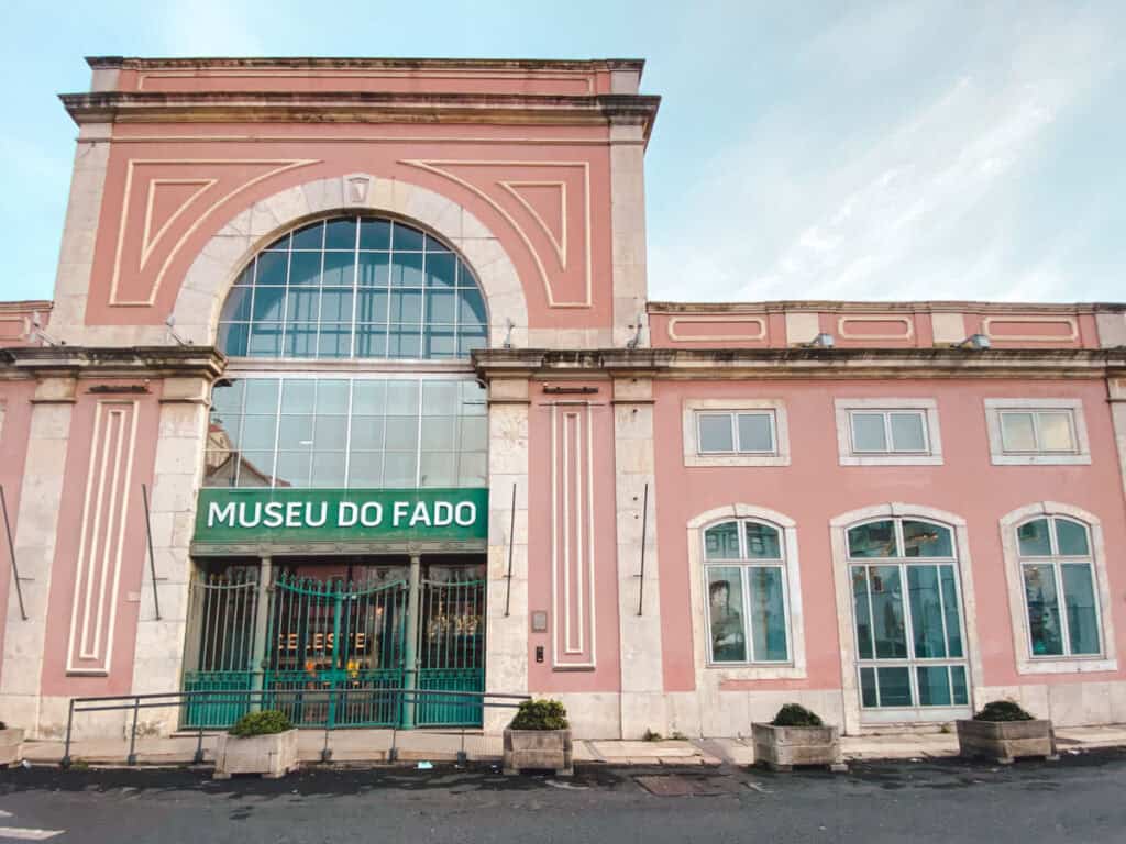 Exterior view of the Fado Museum in Alfama, Lisbon, featuring a grand pink façade with arched windows and a green sign reading 'Museu do Fado.' This cultural landmark highlights the history and significance of Fado music in Portugal.