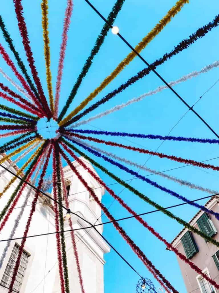 Kleurrijke straten tijdens de Populaire heiligenfeesten in Portugal. Kleurrijke slingers waaieren als een ster uit boven een smalle straat in Lissabon tijdens Festas dos Santos Populares. De blauwe lucht en witte gebouwen maken de feestdecoratie extra opvallend.