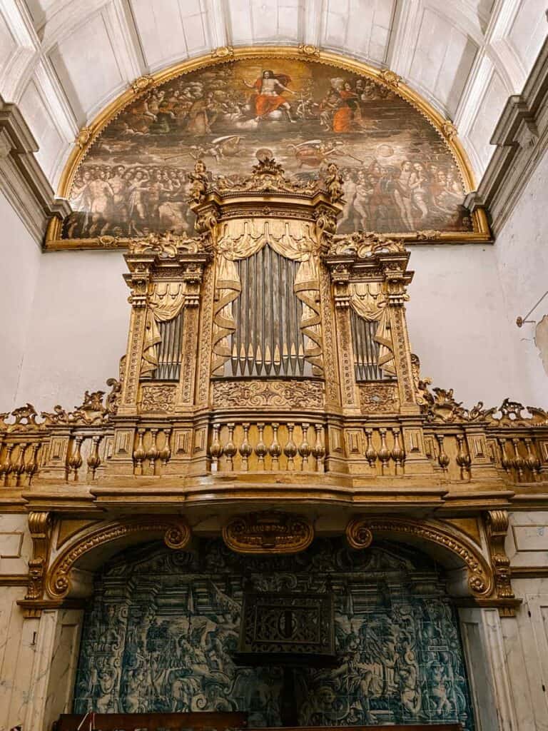 Groot gouden kerkorgel in de Porto Cathedral met rijk houtsnijwerk, geplaatst boven een muur met blauwe azulejo-tegels, onder een halfronde schildering van een religieus tafereel.