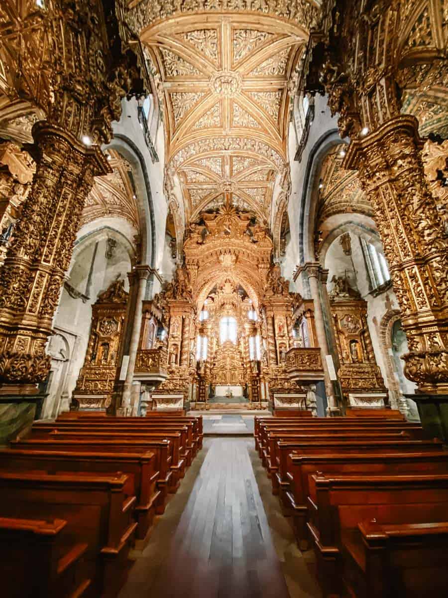 Binnenzicht van de São Francisco Church Porto met gouden details overal, houten kerkbanken en een altaar dat recht uit een sprookje lijkt te komen.