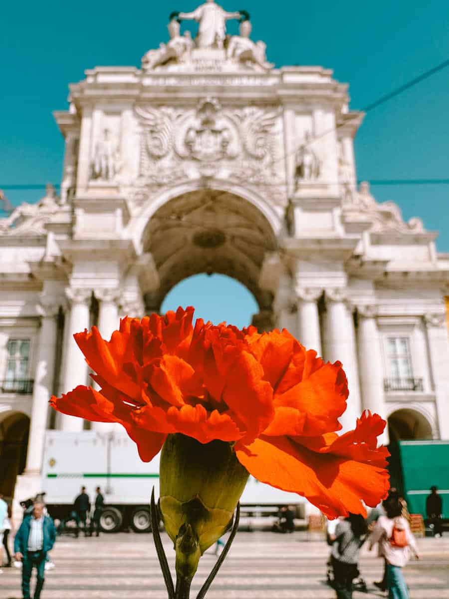 Een felrode anjer wordt vastgehouden voor de Arco da Rua Augusta in Lissabon. De bloem symboliseert de Anjerrevolutie, een belangrijke historische gebeurtenis die in april in Portugal wordt herdacht.
