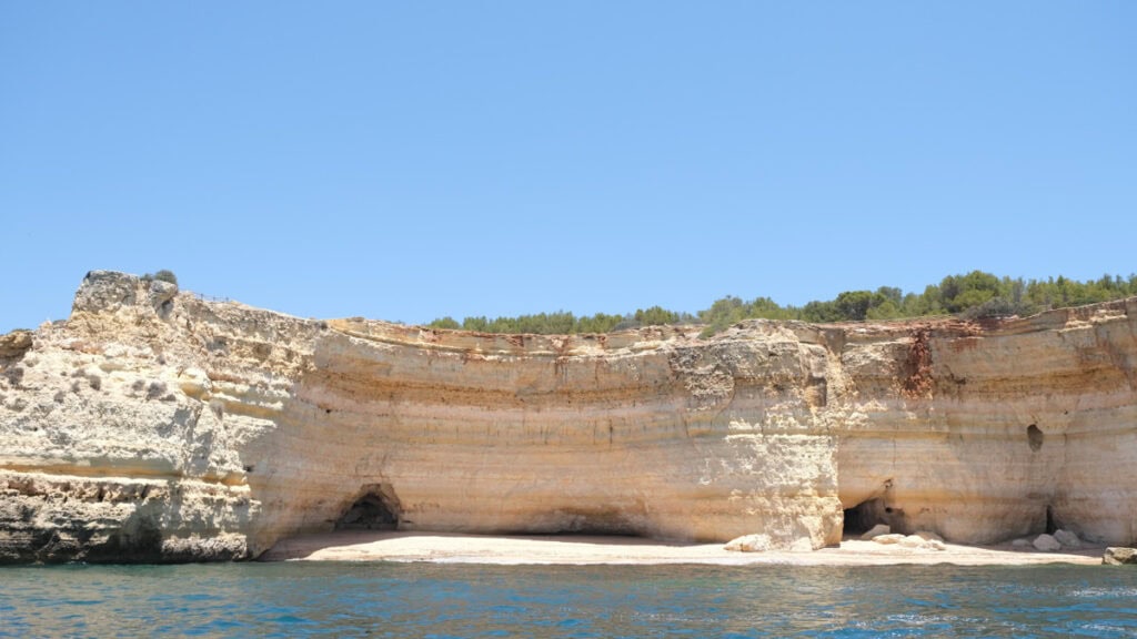 Uitzicht op een rustige inham en zandstrand met lichte rotswanden vanaf zee tijdens een Benagil boat tour langs de kust van de Algarve.
