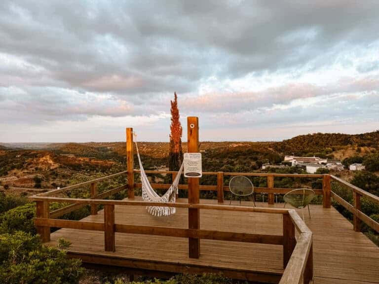 Uitzicht vanaf het houten terras met hangmat en stoelen bij Hotel Rural Quinta do Marco, omringd door de heuvels van de Algarve bij zonsondergang.