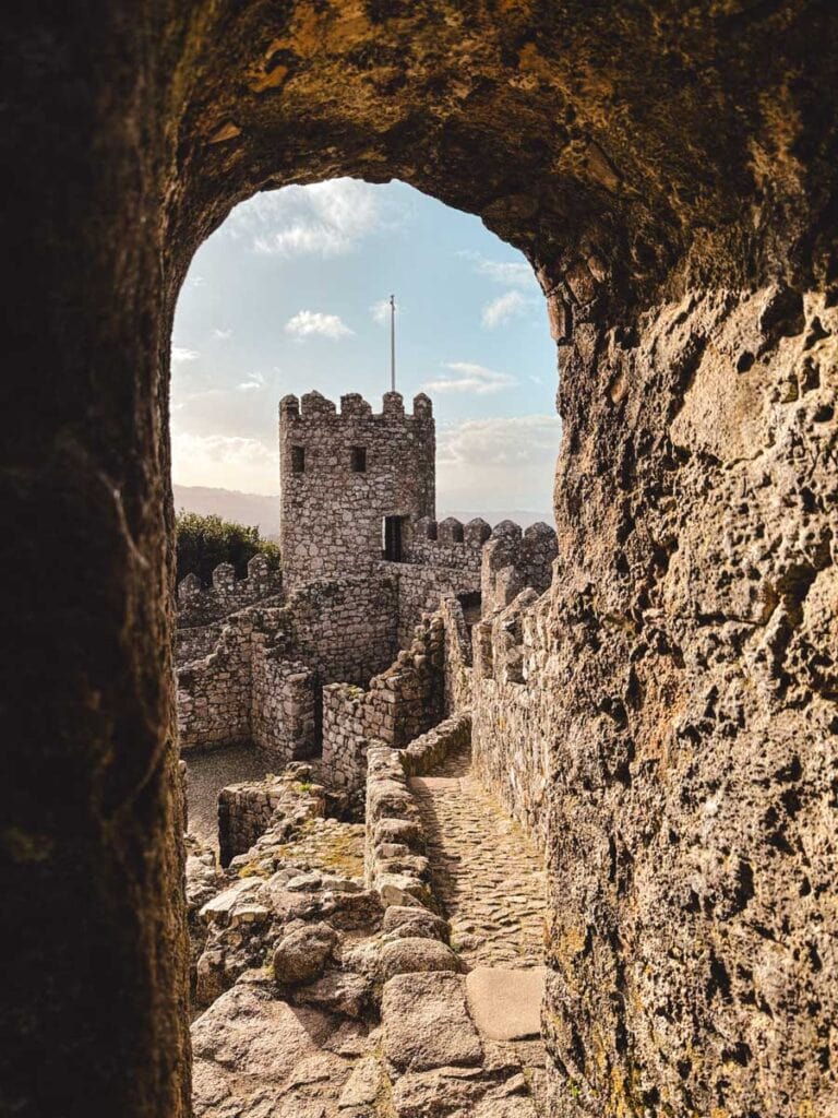 Uitzicht op het Moors kasteel in Sintra door een stenen boog, met kronkelende paden en verdedigingsmuren op de voorgrond.