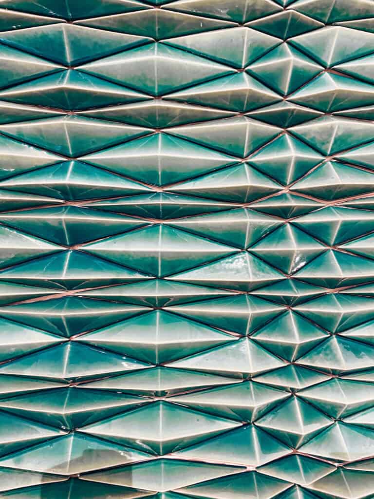 Painel de azulejos tridimensionais em tons de verde e azul com formas geométricas repetidas e acabamento brilhante no Museu do Azulejo. A visita ao museu é uma boa opção para conhecer a tradição dos azulejos em Lisboa quando chove.