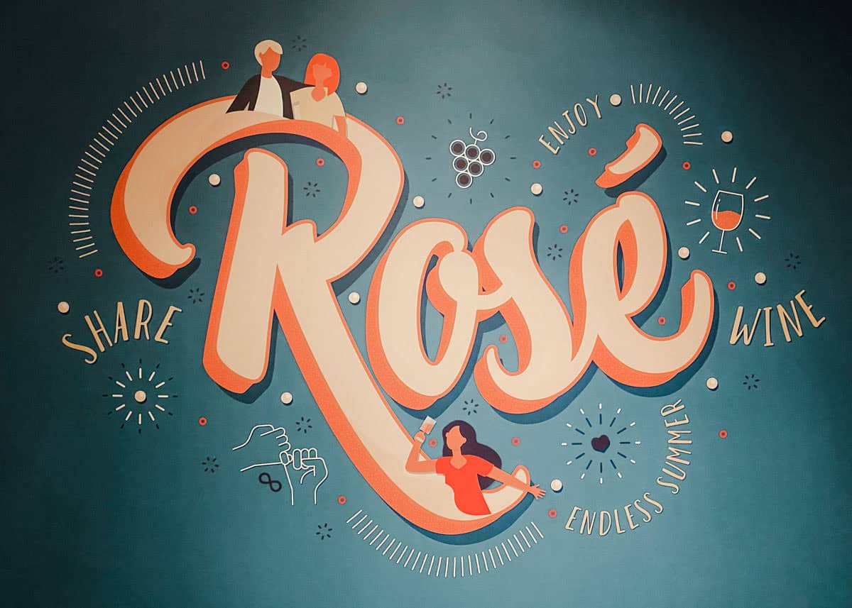 Mural artwork at the Pink Palace Porto featuring bold lettering of the word Rosé, surrounded by playful drawings of people, grapes, and a wine glass with the phrases Share, Enjoy, Endless Summer, and Wine.