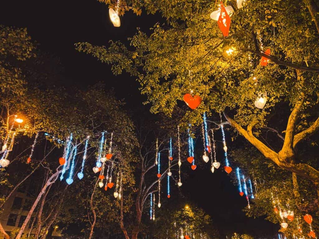 Glowing red and white heart-shaped ornaments and cascading icicle lights hang from tree branches on Avenida da Liberdade in Lisbon, creating a dreamy canopy effect. This romantic and unconventional setup adds a playful twist to traditional Christmas decorations in Lisbon.