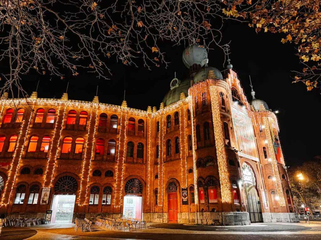 The red-brick Campo Pequeno building in Lisbon is outlined with cascading golden Christmas lights, with glowing windows and festive signage at its main entrance. This striking display brings festive flair to a historic venue and expands the reach of Lisbon Christmas lights beyond the city centre.