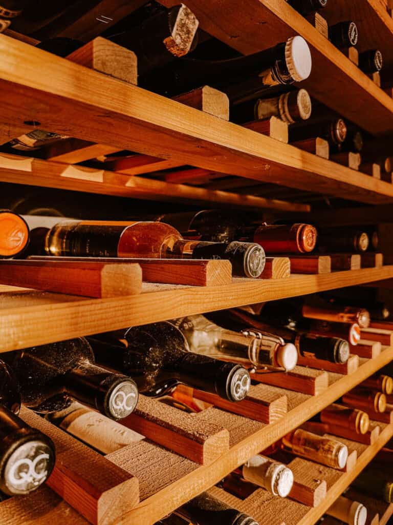 A variety of wine and champagne bottles displayed on a wooden shelf, including a prominently featured bottle of Champagne Mathelin. Captures the diverse offerings found in wine shops during a Carcavelos wine tasting or Lisbon vineyard visit.