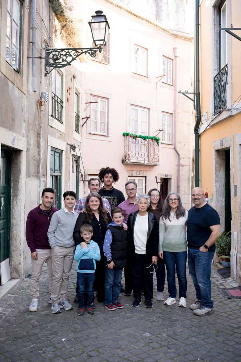 Een grote familie poseert samen in een smal, sfeervol straatje in Lissabon, omringd door kleurrijke gebouwen en klassieke straatlantaarns. De ontspannen groepsfoto straalt verbondenheid uit en legt een dierbaar moment vast tijdens hun familiereünie in de stad.