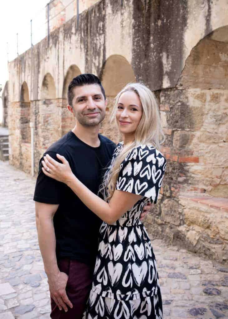Een stel poseert dicht tegen elkaar aan in een charmant, oud steegje met stenen muren en bogen in Lissabon. Hun ontspannen houding en de historische setting benadrukken de intieme sfeer van een fotoshoot in Lissabon.