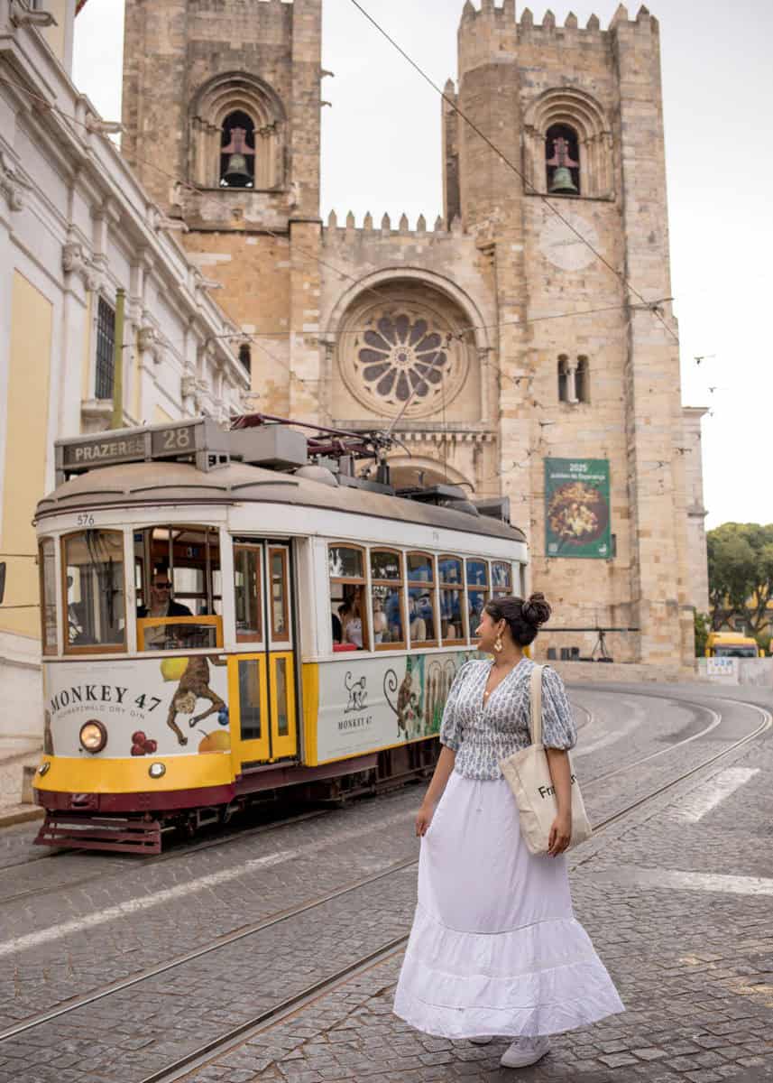 Een vrouw in een witte rok kijkt naar de iconische gele tram 28 die voorbijrijdt voor de Sé kathedraal in Lissabon. De combinatie van historische architectuur en lokaal straatbeeld maakt deze foto tot een klassiek moment tijdens een stadsfotoshoot in Lissabon.