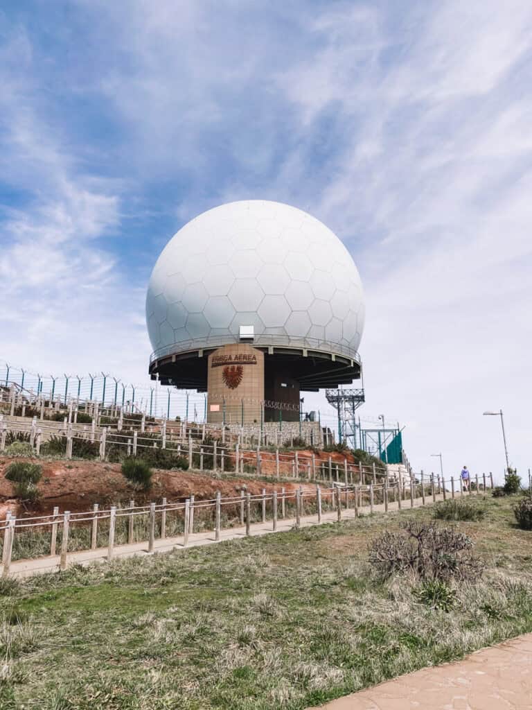 Radarstation bij Pico do Arieiro op Madeira, met een grote witte radarkoepel op de bergtop. Op de voorgrond loopt een wandelpad langs hekken en struiken.