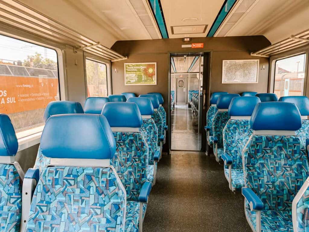 Interior of the Algarve Train Line carriage with rows of blue patterned seats and large windows showing the sunny landscape outside.
