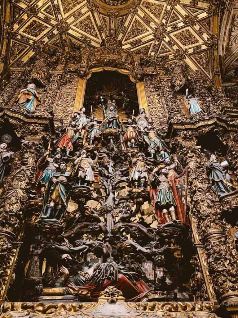 Retábulo de Jessé no Porto ricamente talhado em madeira dourada, com várias figuras bíblicas dispostas em camadas ao redor de uma árvore central que se eleva até o topo. O teto ornamentado e os detalhes esculpidos criam uma cena dramática e densa que destaca a grandiosidade do barroco dentro da igreja.