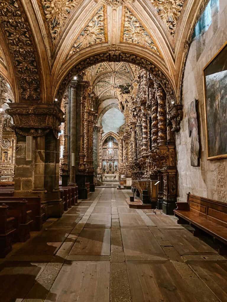 Capela da família Brandão no Porto com corredor lateral revestido de talha dourada e colunas esculpidas ao longo das paredes. O arco trabalhado no teto conduz o olhar até o altar ao fundo, destacando a riqueza barroca e a profundidade do espaço interior.