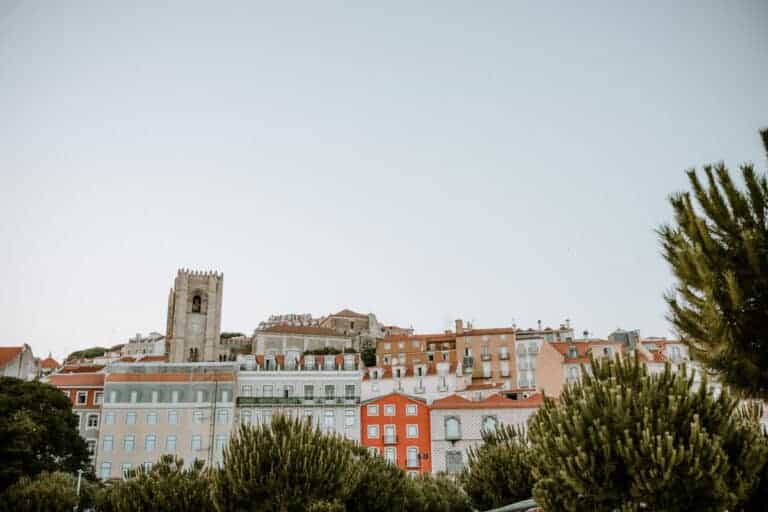 Vista panorâmica de Alfama com prédios coloridos e telhados de terracota espalhados pela encosta de Lisboa. A torre da Sé de Lisboa aparece ao fundo entre o casario e ajuda a situar um dos principais pontos de interesse para quem procura o que fazer em Alfama.