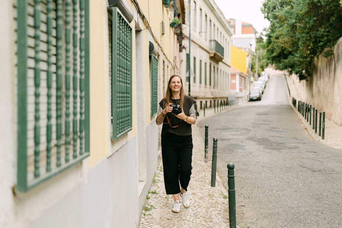 Fotograaf in Lissabon tijdens een shoot, wandelend met haar camera door een rustige straat.