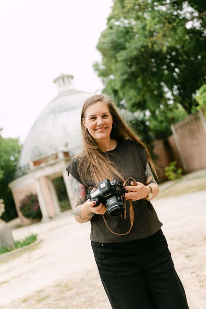 Marga, fotograaf in Lissabon, staat glimlachend met haar camera in een groene stadstuin.