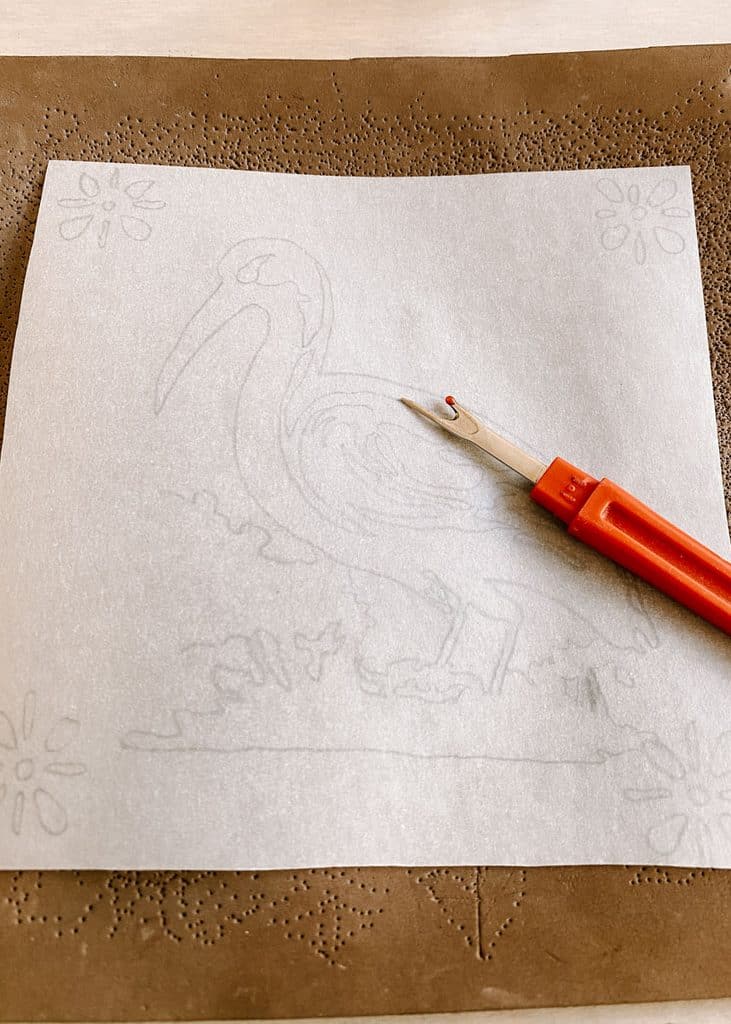 A sheet of tracing paper with a pencilled bird and floral design lies over a perforated pattern with a red handled tracing tool resting on top. The design is being prepared during a tile painting workshop in Lisbon.