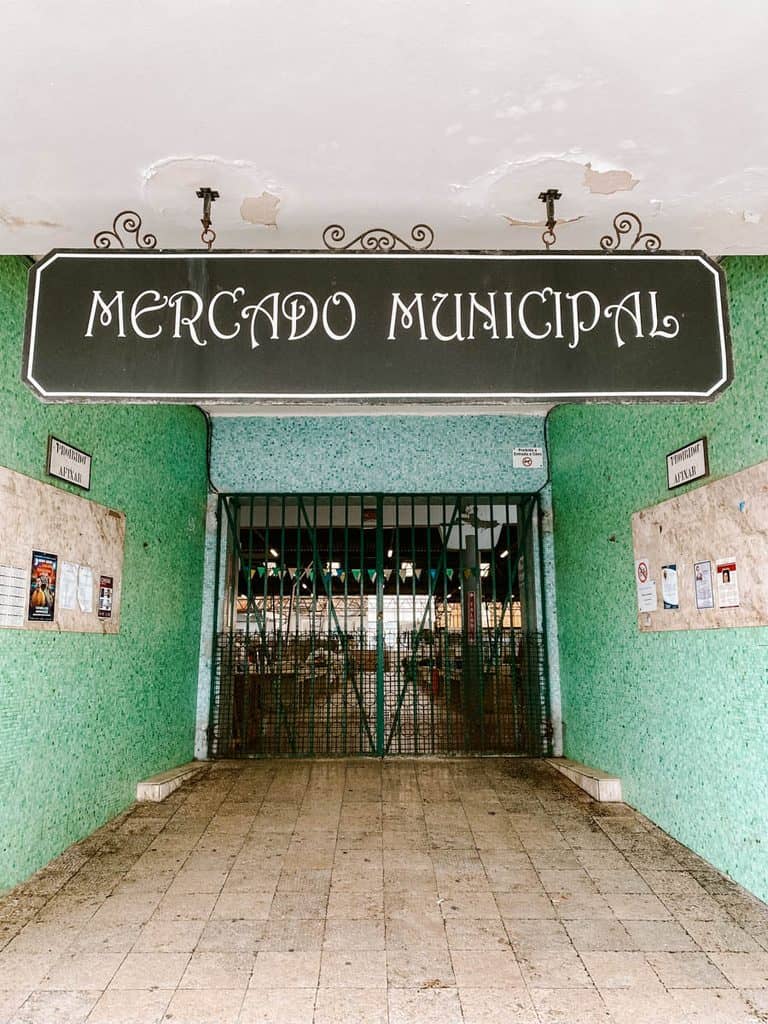 De ingang van de Mercado Municipal in Nazaré met groene mozaïektegels op de muren en een groot zwart bord met de tekst "MERCADO MUNICIPAL". Een gesloten groen metalen hek geeft toegang tot de overdekte markthal.